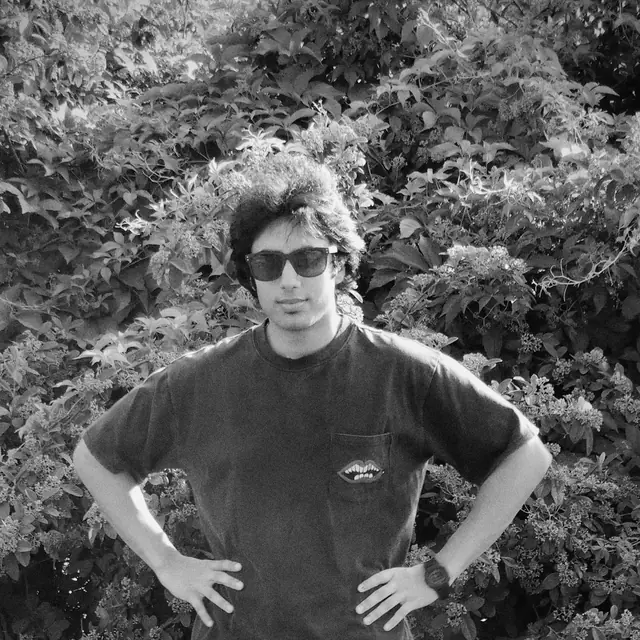 Mohd Shayan in sunglasses, hands on his hips, in front of a flowering hedge